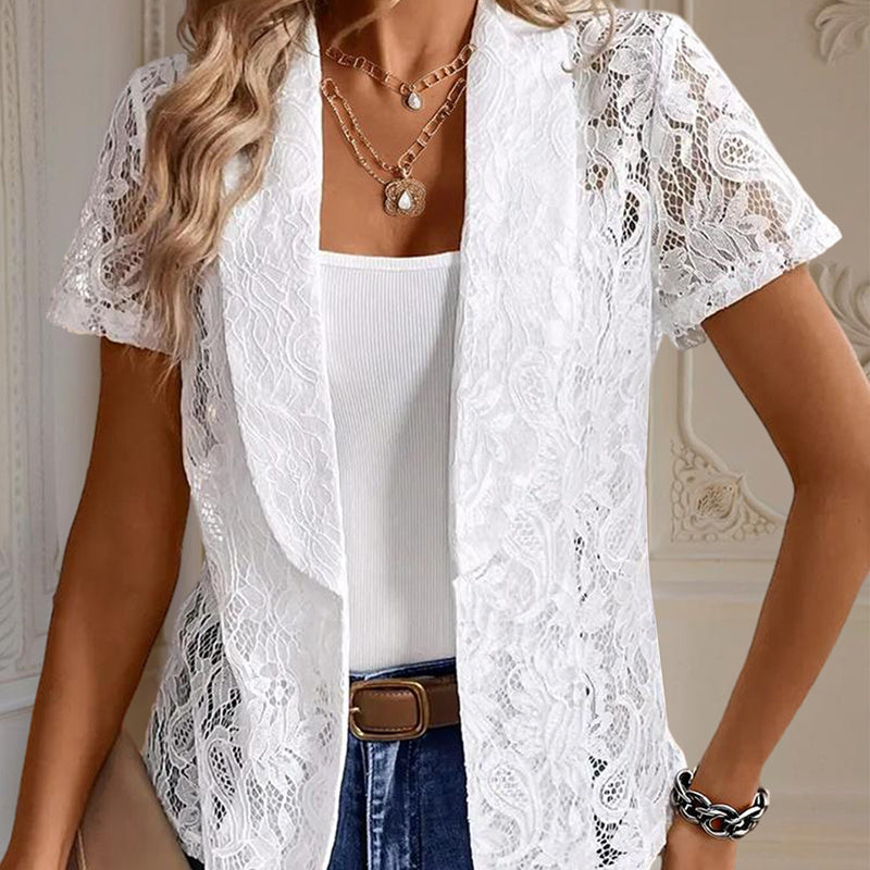 Woman wearing a white lace top over a white shirt with blue jeans indoors.