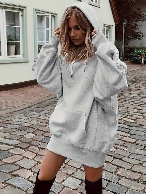 Woman wearing a gray hoodie dress on a cobblestone street.