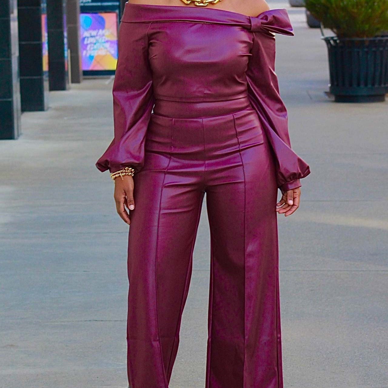 Person wearing a burgundy off-shoulder top and high-waisted pants in an outdoor setting.